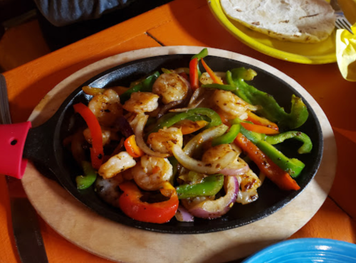 Sizzling shrimp fajitas with colorful bell peppers and onions on a hot skillet, served with tortillas.